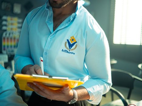 Man in professional attire holding a yellow notepad and pen in an office setting, depicted clearly with branding. 34007237