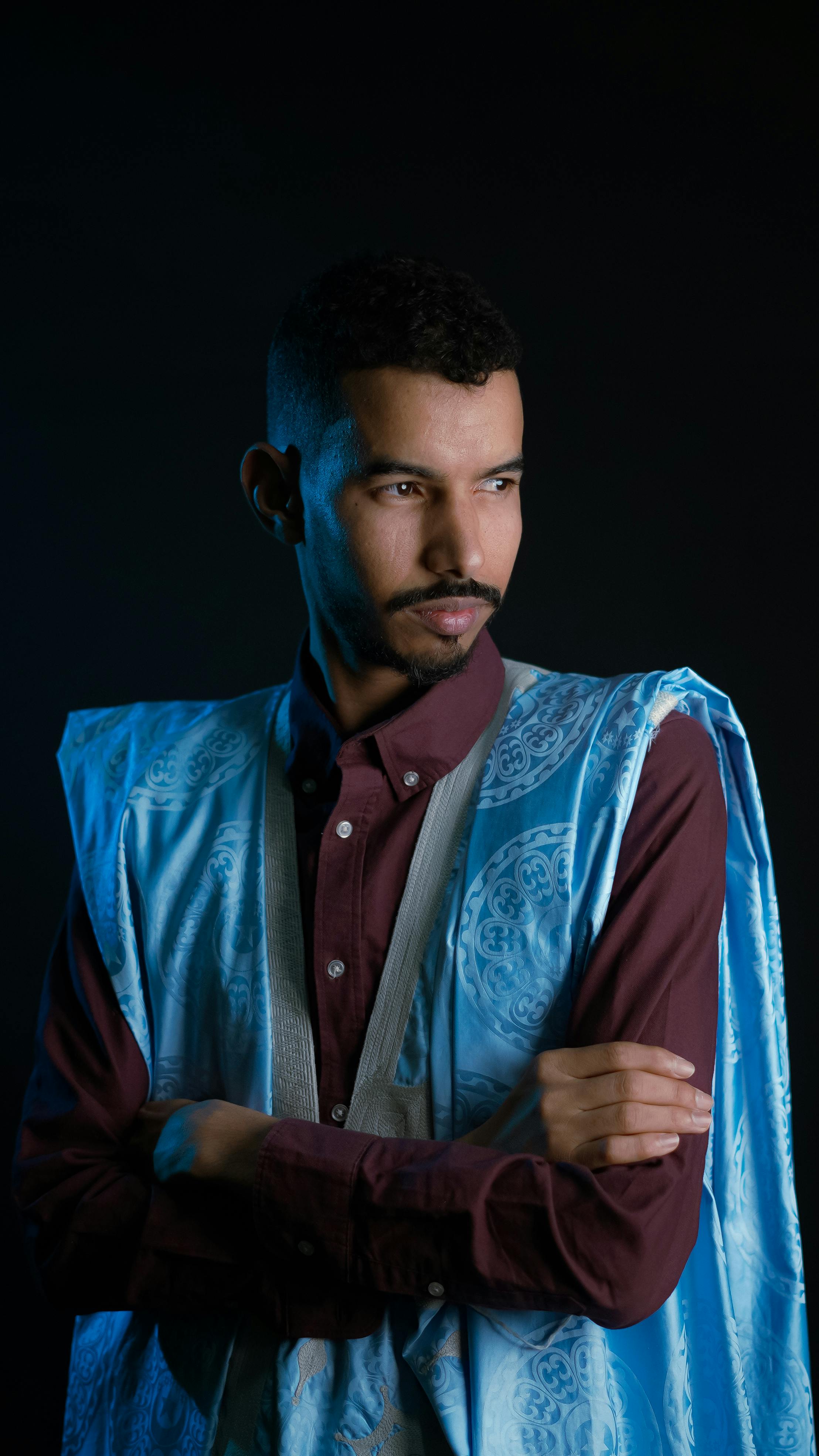 Portrait of a man in vibrant traditional clothing against a dark background, exuding confidence.
