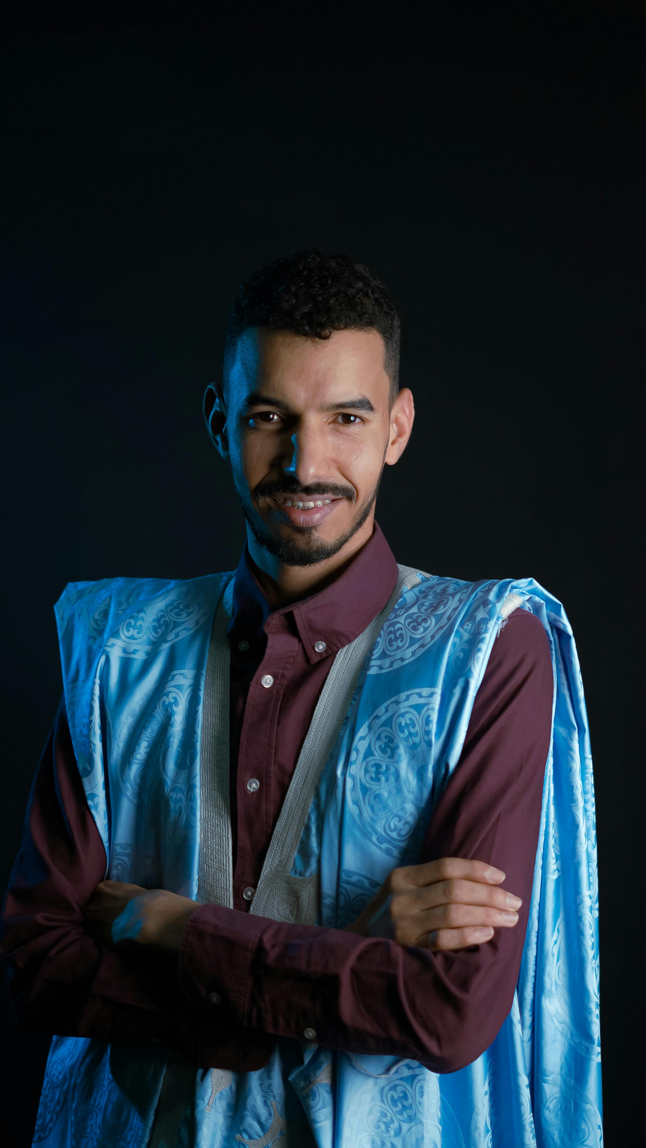 Studio portrait of a man in traditional blue attire. Moody lighting enhances the cultural and stylish look.