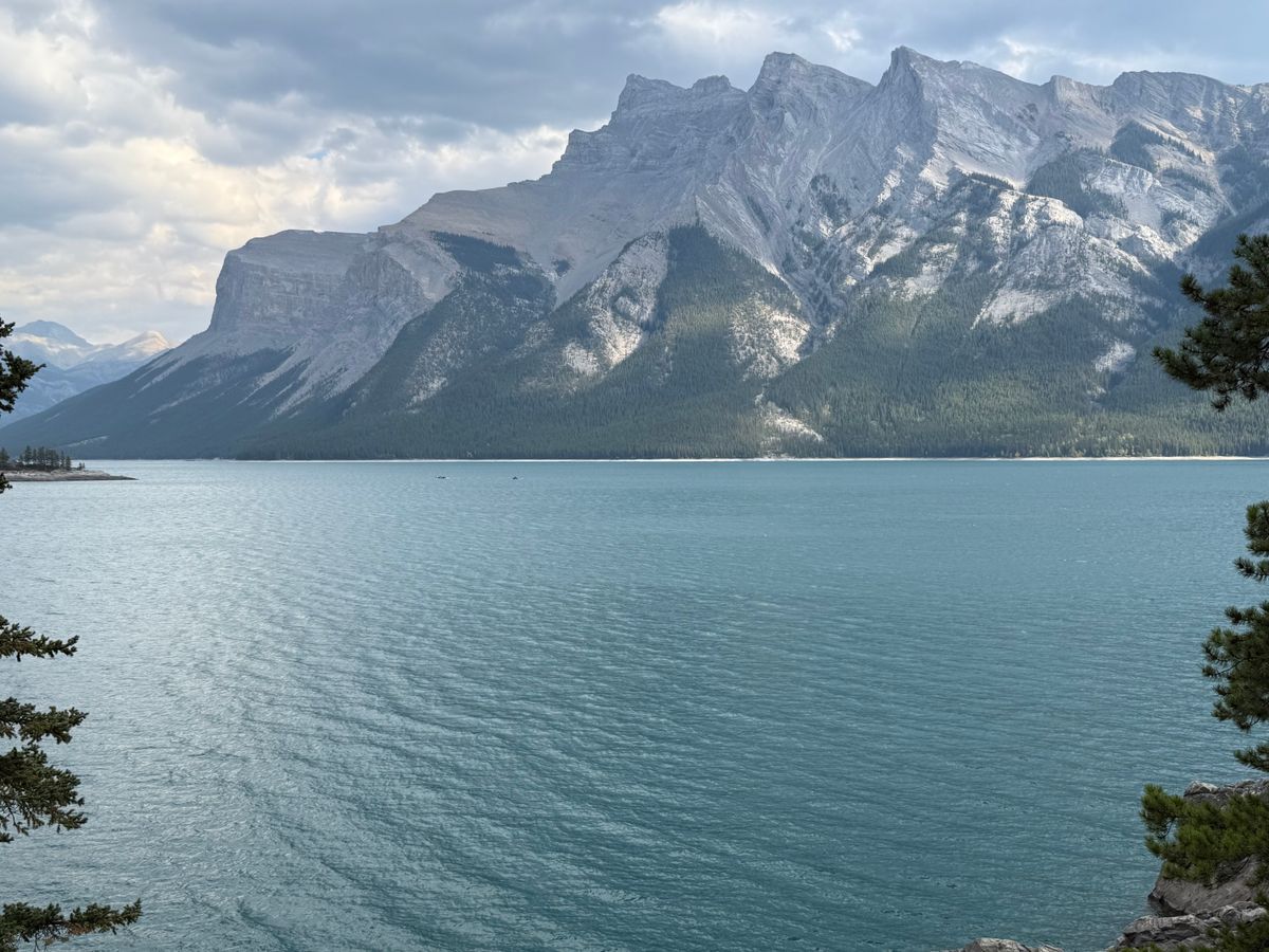 Stunning vista of Lake Minnewanka surrounded by majestic Rocky Mountains under a cloudy sky.