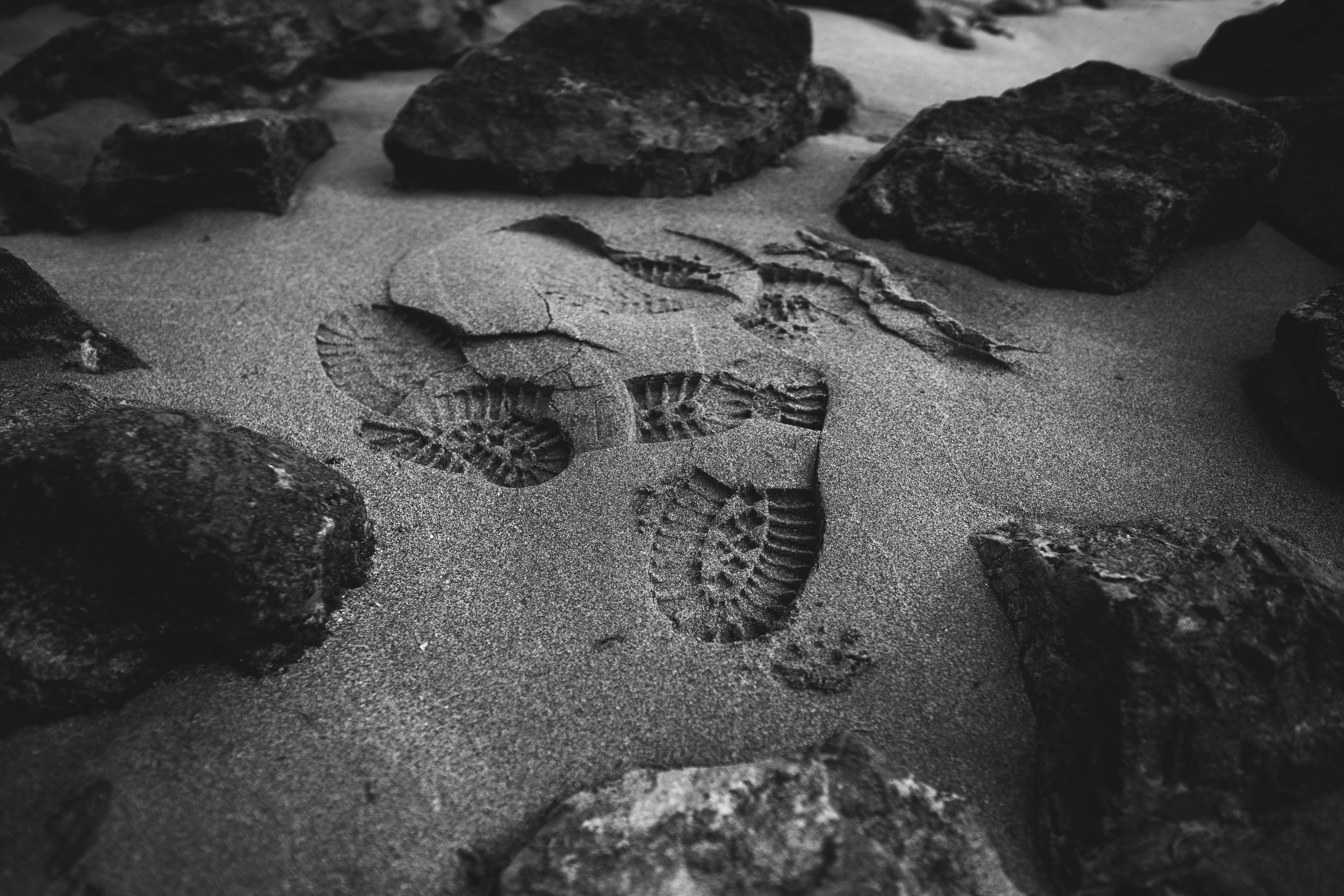 Monochrome close-up of footprints on a sandy beach surrounded by rocks.