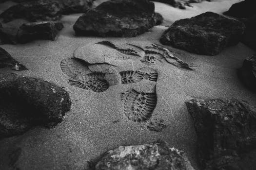 Monochrome close-up of footprints on a sandy beach surrounded by rocks.