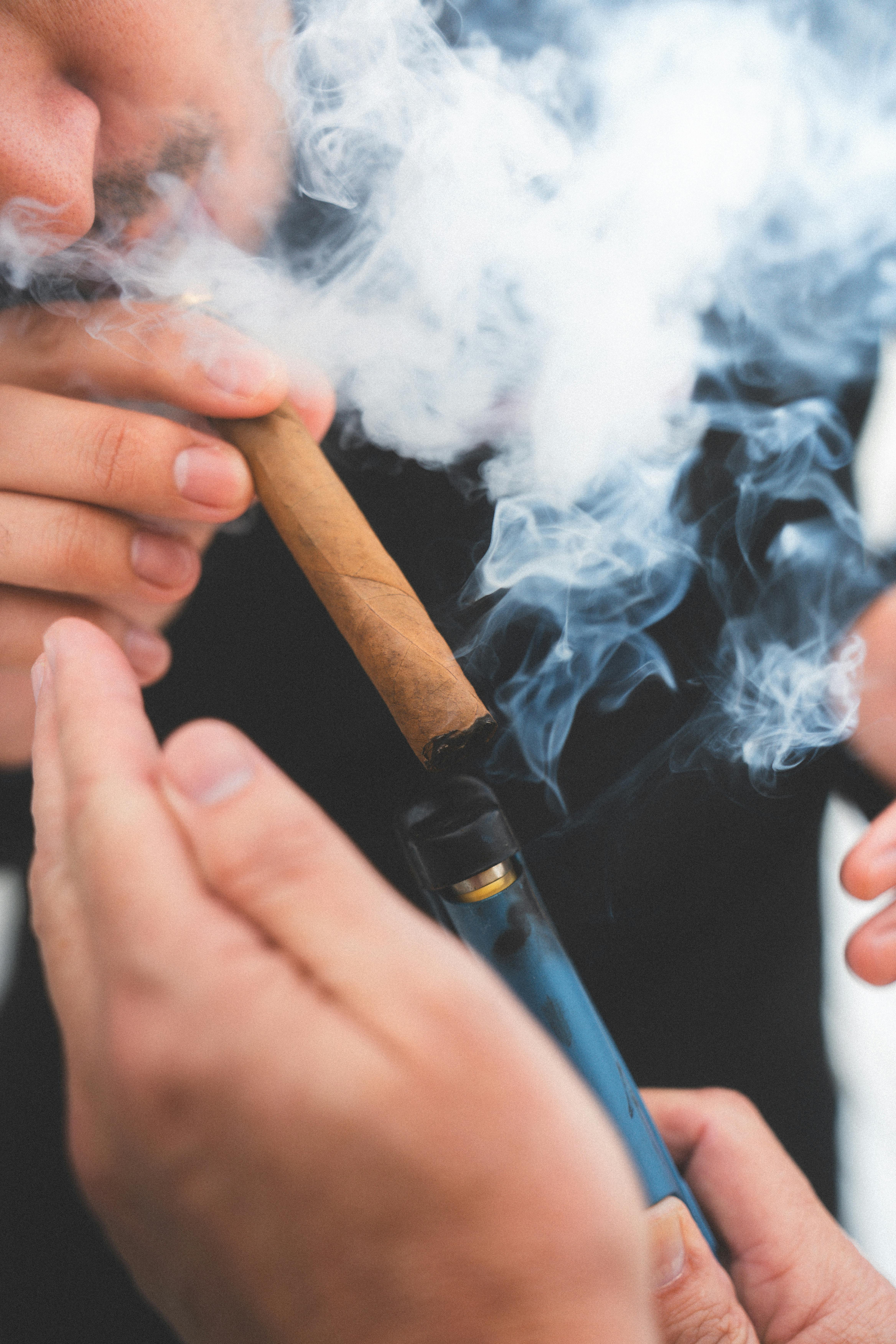 A person lighting a cigar, surrounded by smoke, close-up view.