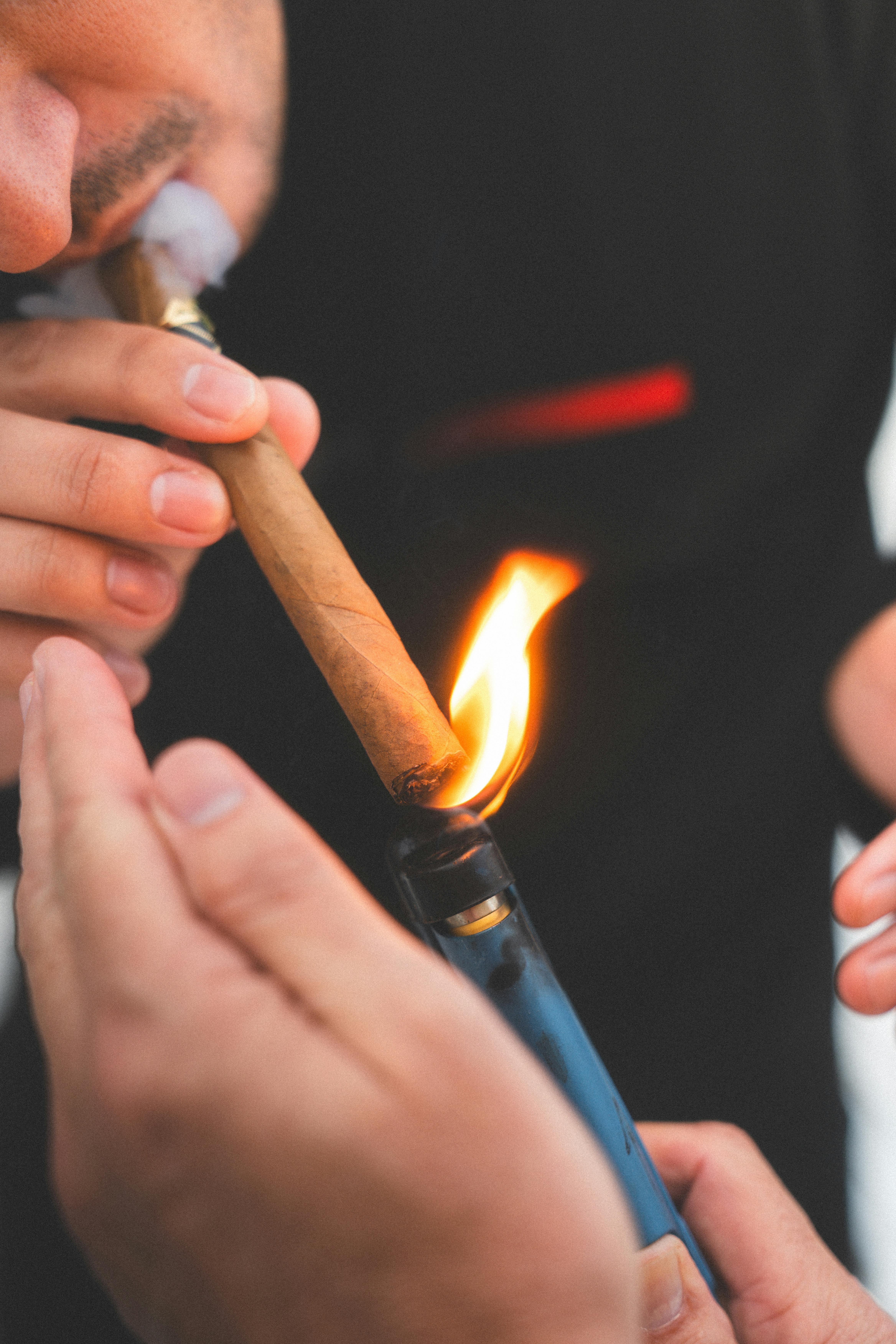 Close-up of a man lighting a cigar with a lighter outdoors during the day.