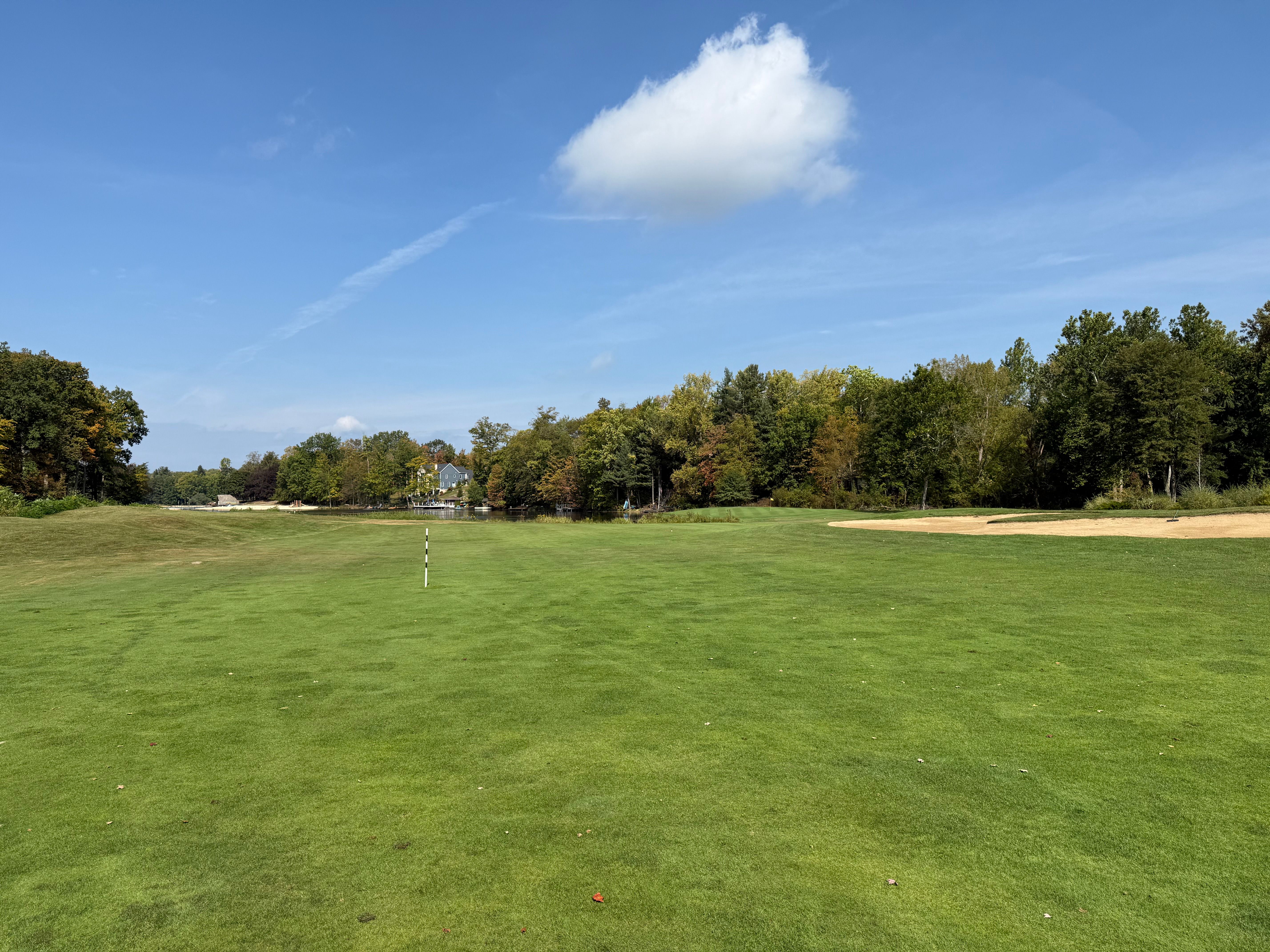 Expansive green golf course under a clear blue sky, with trees lining the edges.