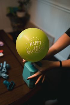 Person inflating a green balloon with 'Happy Birthday' text indoors.