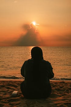 A peaceful silhouette of a woman on Kuantan Beach during a golden sunrise.