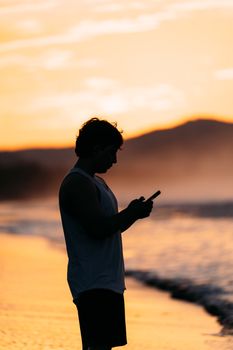 Captivating silhouette of a person using their phone by the beach at sunset in El Salvador.
