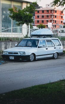 A classic white station wagon parked on an urban street with a rooftop cargo box.
