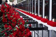 A solemn memorial wall adorned with red carnations and candles during the daytime.