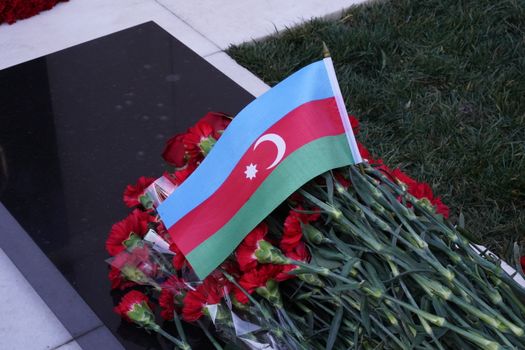Red flowers and Azerbaijani flag lie solemnly at a gravesite monument.