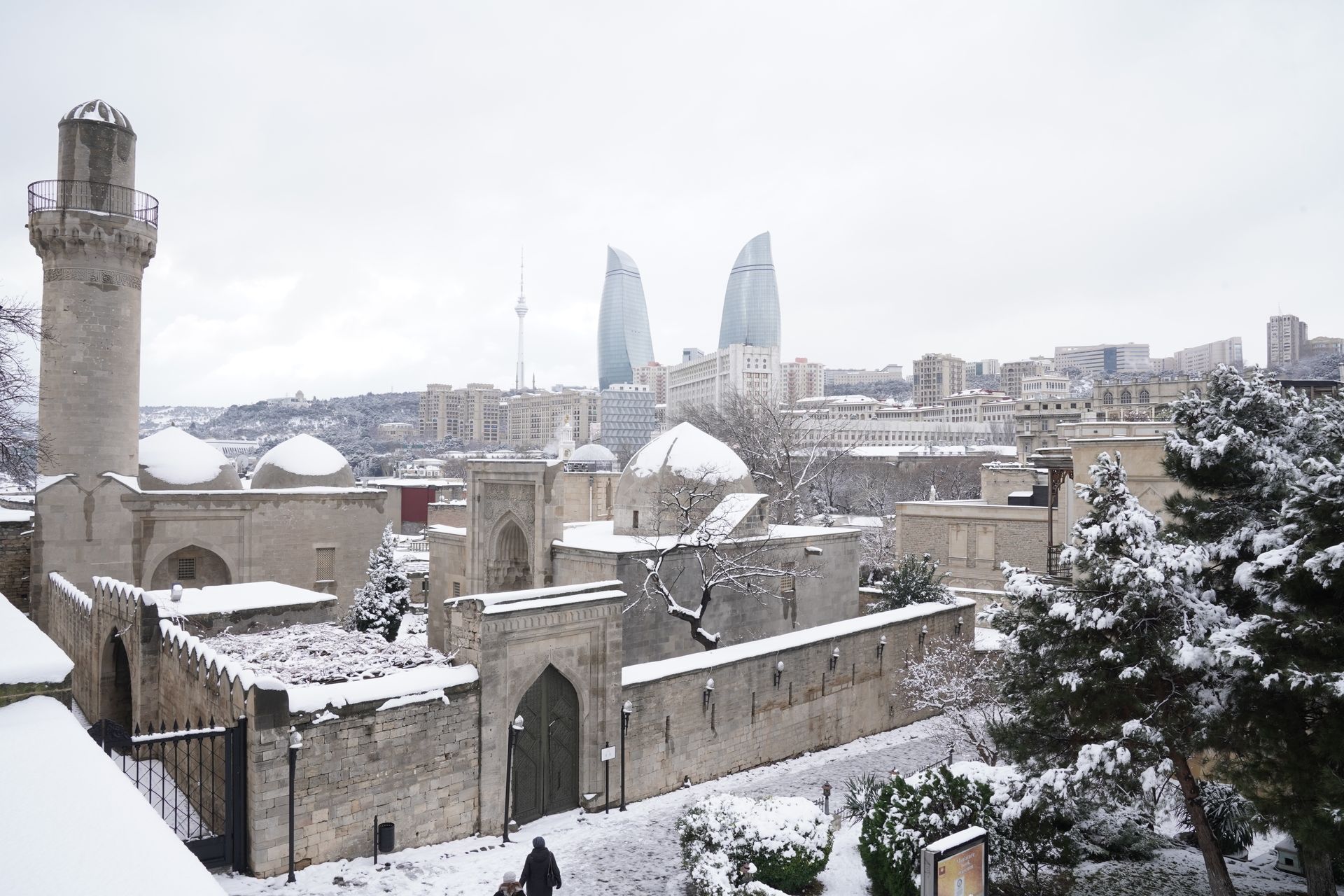 A snowy landscape of Baku featuring the historic Old City and modern Flame Towers in the background.