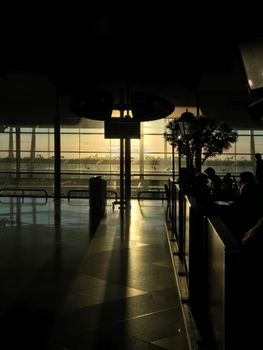 Silhouetted travelers in an airport terminal during a serene sunset, casting long shadows.