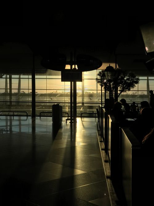 Free Silhouetted travelers in an airport terminal during a serene sunset, casting long shadows. Stock Photo