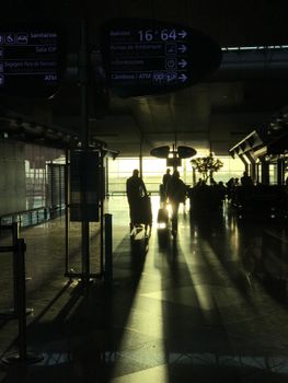 Silhouette of travelers walking in an airport terminal with sunlight streaming in.