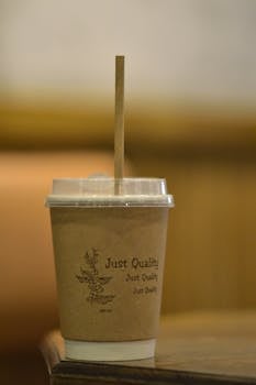 Close-up of a paper coffee cup labeled 'Just Quality' with a wooden straw