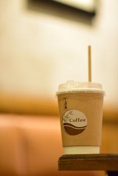 A brown eco-friendly coffee cup with a straw on a wooden table indoors.