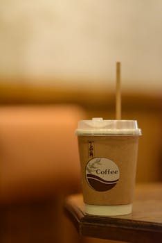 A biodegradable coffee cup with a wooden straw on a table in a cozy indoor cafe setting.