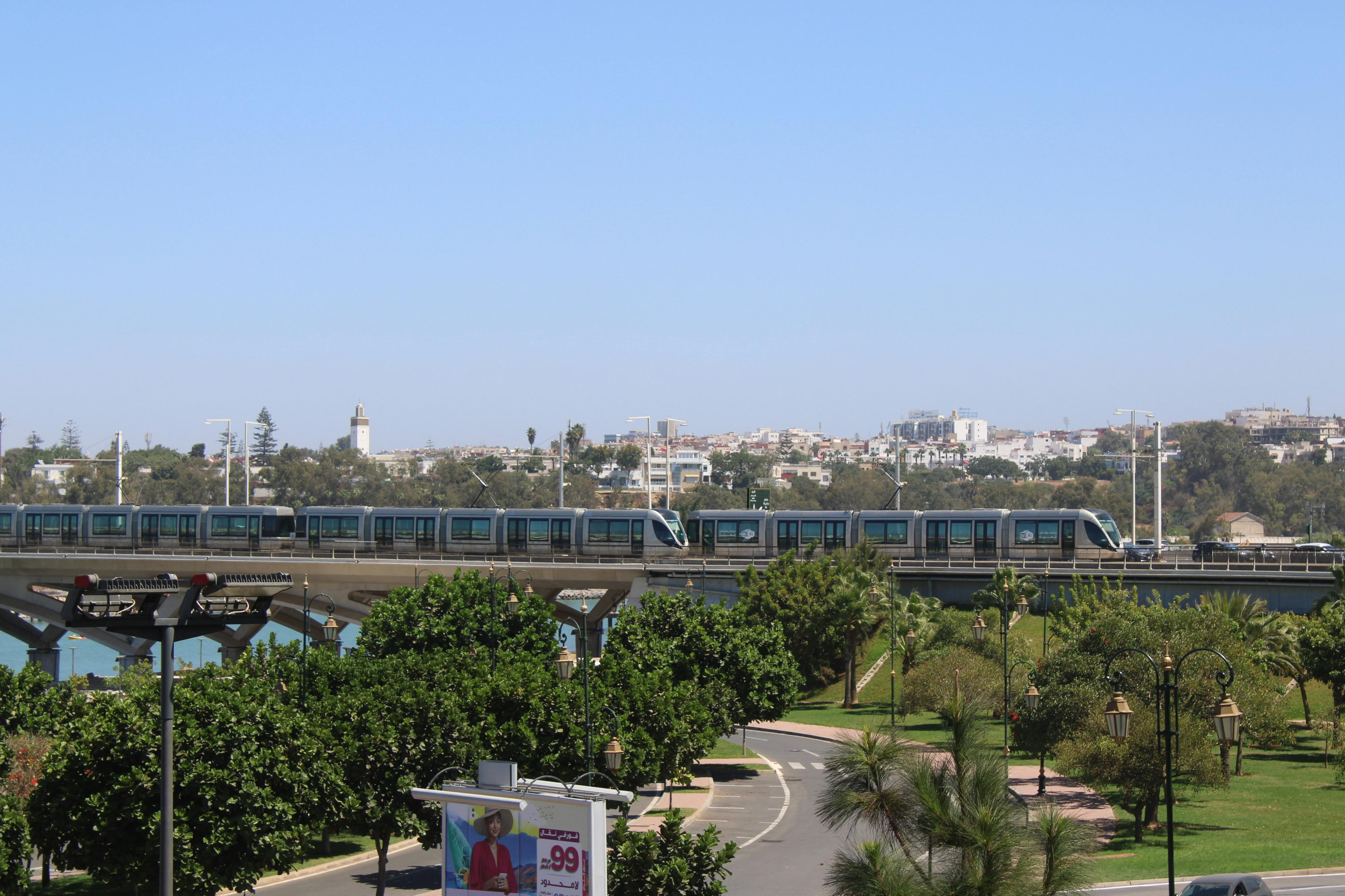 A modern tram travels over a scenic bridge with a cityscape backdrop in Rabat, Morocco.