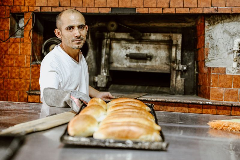 A skilled baker in a traditional bakery presents a tray of freshly baked bread loaves.