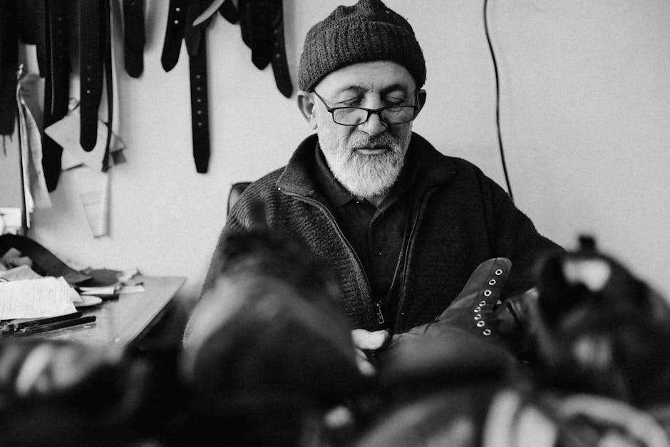 Mitä yhtiö tekee ja kenelle? Mitä yhtiö tekee ja kenelle? - Black and white photo capturing an elderly man crafting leather shoes in a workshop.