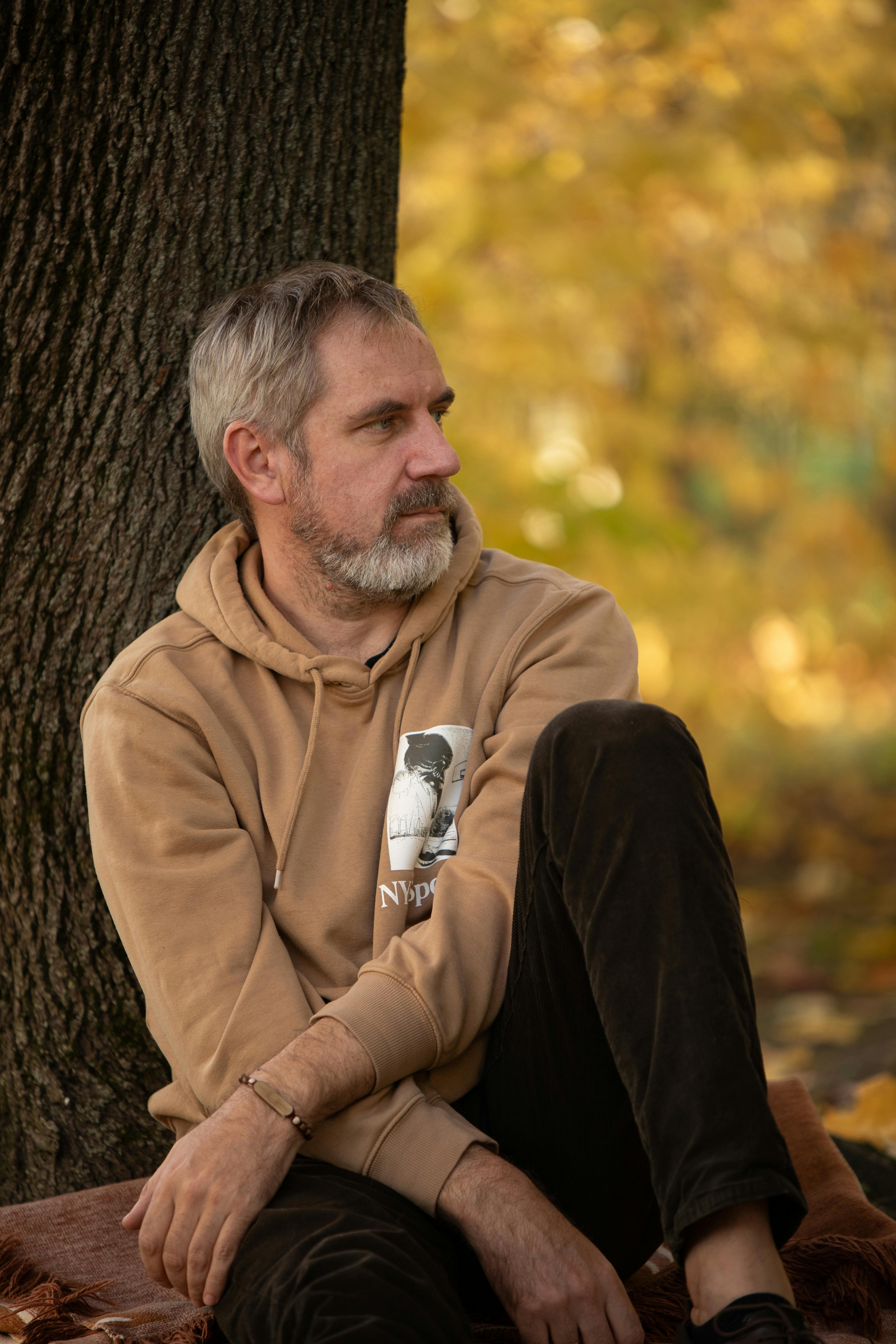 Pensive man sitting against a tree enjoying the autumn scenery in a park.