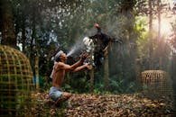 在泰国一片绿树成荫、阳光明媚的森林里，一名男子正愉快地与一只公鸡互动，捕捉到了一个文化时刻