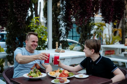 Free Father and son clink glasses over food and drinks outdoors, enjoying a summer meal together. Stock Photo