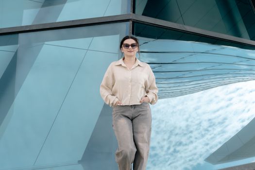 Confident woman in casual attire posing in front of modern geometric glass architecture.