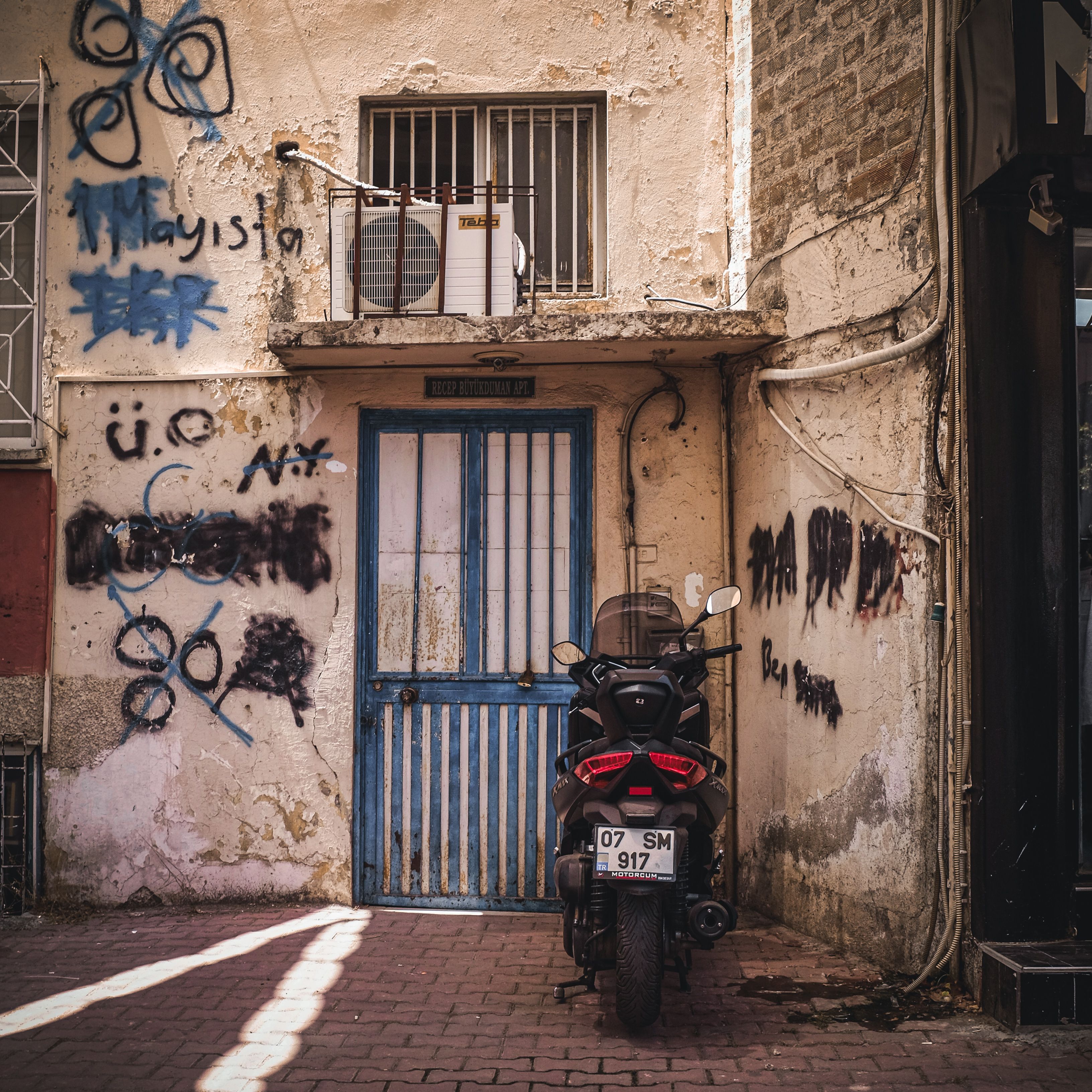 A motorcycle parked in a narrow alleyway with graffiti and a blue door, conveying urban street vibe.