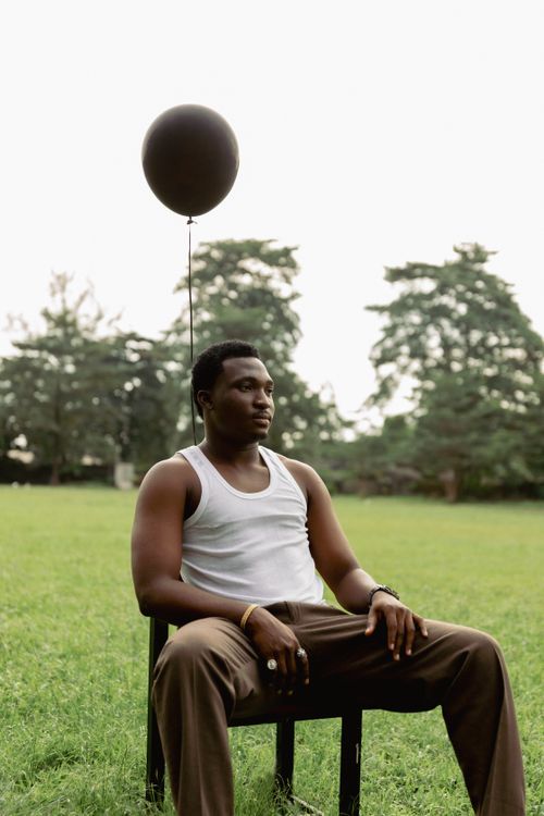 Free Man sitting on a chair in a park holding a black balloon. Stock Photo