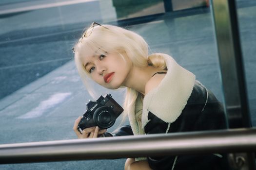 Blonde woman holding vintage camera, urban outdoor setting.