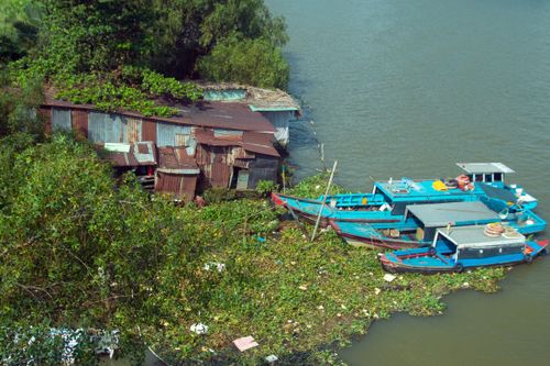 Free Colorful boats docked beside a rustic riverside shack surrounded by lush greenery. Stock Photo