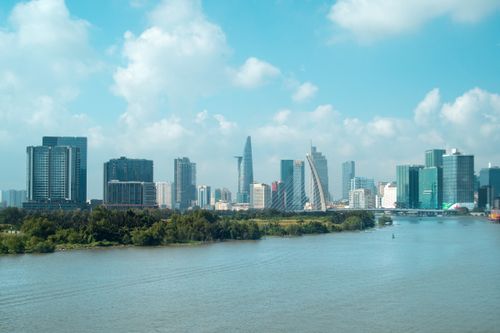 Free Vibrant Ho Chi Minh City skyline view with skyscrapers and river foreground under a bright blue sky. Stock Photo