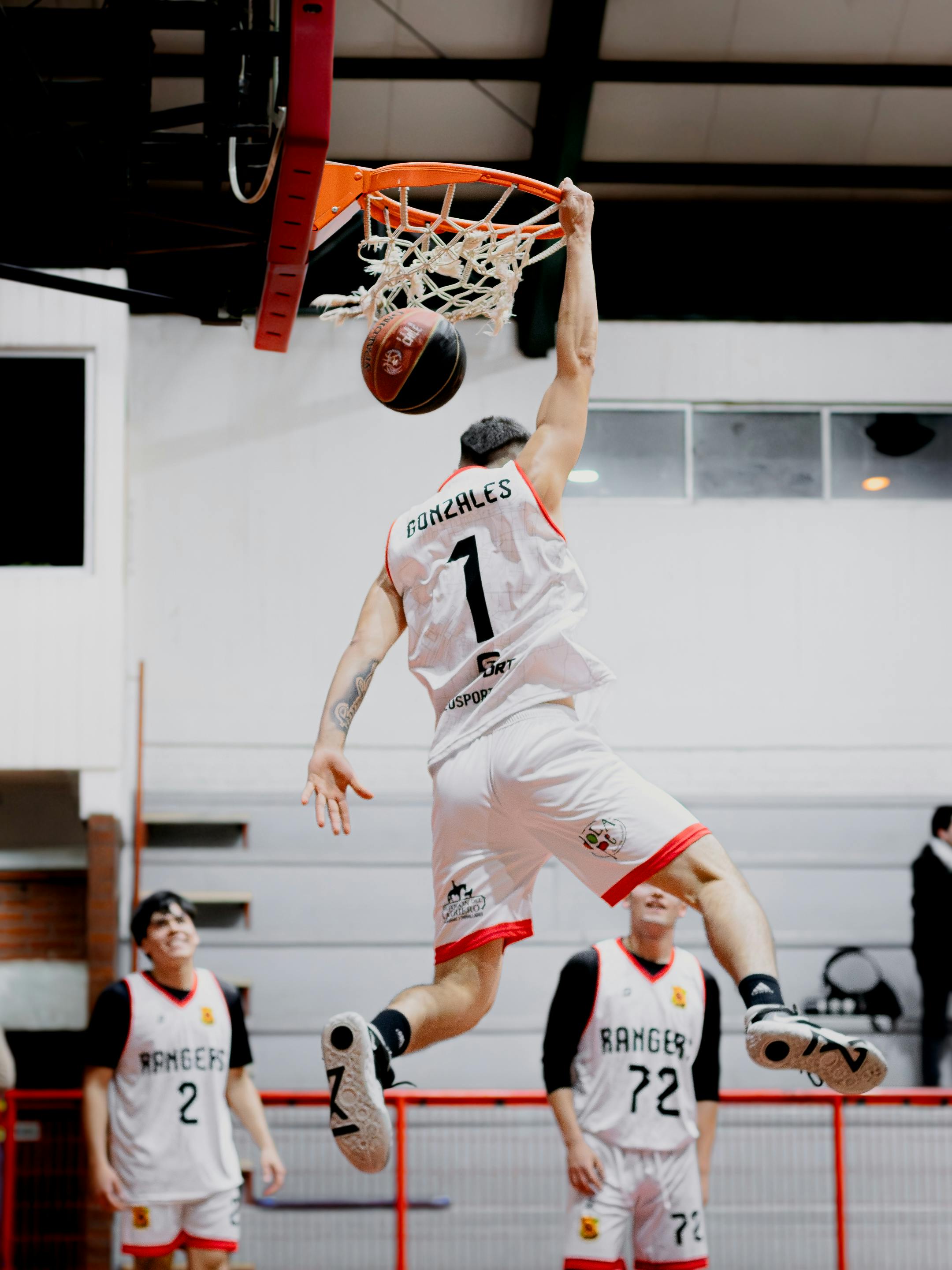Dynamic shot of a basketball player performing a slam dunk during an indoor game.