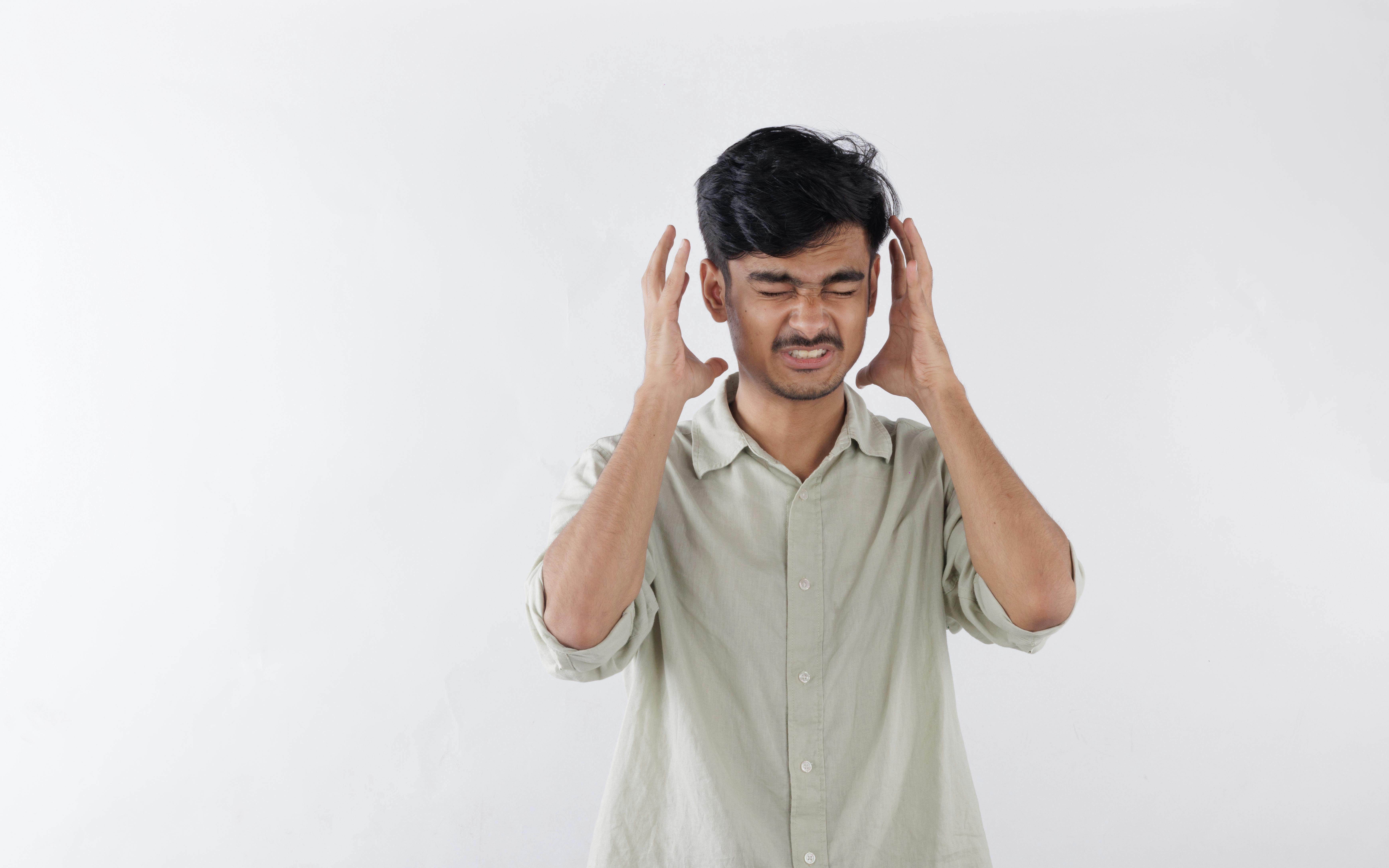 Young man expressing frustration, hands on head, isolated background.