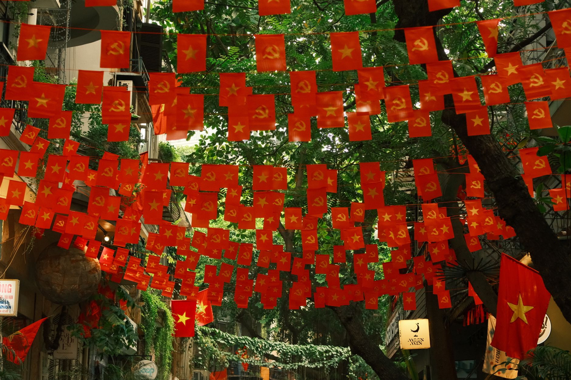 A vibrant display of red flags with yellow stars and communist symbols over a street in Hanoi, Vietnam.