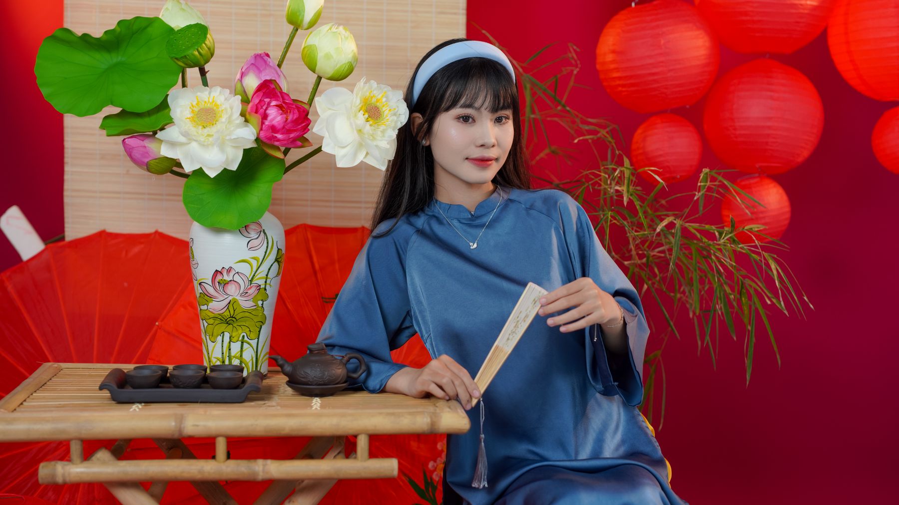Woman in traditional attire with flowers and red lanterns in an elegant tea ceremony setup.
