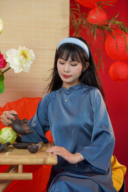 Free Young woman in blue dress pouring tea in a tranquil setting with flowers. Stock Photo