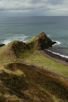 A stunning aerial view of the rugged coastline of Giant's Causeway, showcasing lush green hills and deep blue ocean.