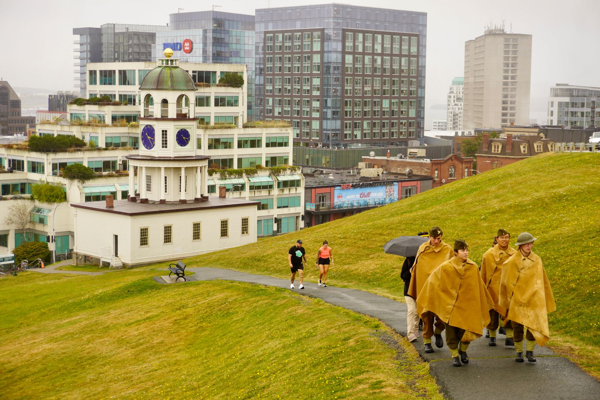 Historic Halifax Clock Tower with people walking on Citadel Hill, cityscape backdrop, rainy day.