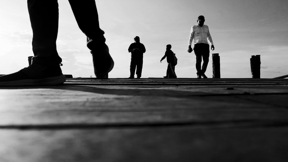 Black and white shot of silhouetted people walking on a dock in Georgetown at sunset.