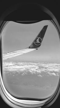 Black and white view of an airplane wing over clouds seen through a window.