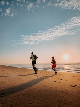 Two people jogging along a sandy beach at sunrise creating a serene and motivational scene.