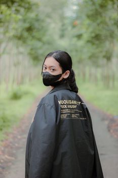 A person wearing a black jacket and mask stands on a tree-lined path.