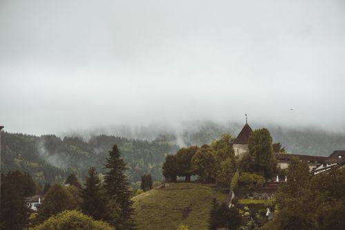 Free Misty landscape with Gruyères Castle amidst green hills and forested mountains, Switzerland. Stock Photo
