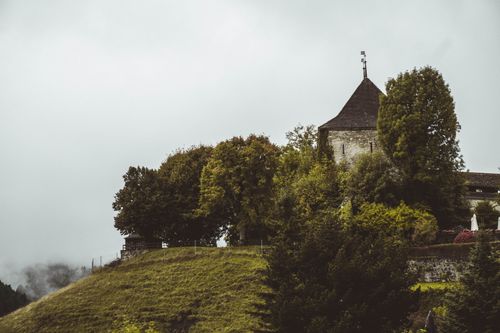Free Beautiful view of a medieval castle surrounded by lush green trees in Gruyères, Switzerland. Stock Photo