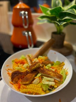 A vibrant fresh salad with chicken strips, carrot, corn, and lettuce.