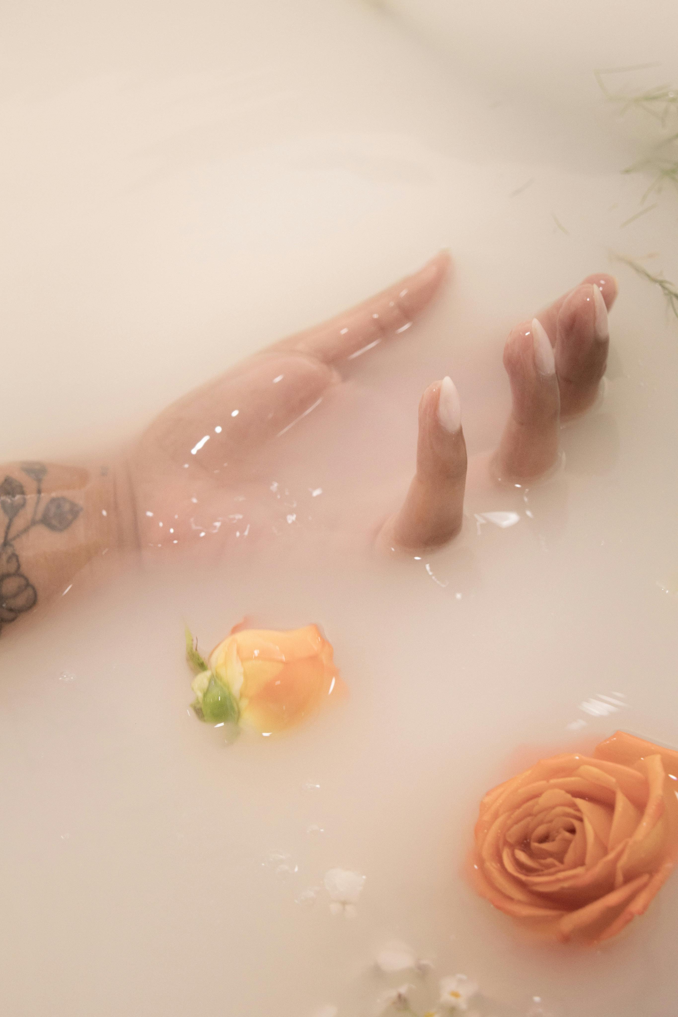 Tattooed hand with rose in ethereal milky bath. Serene and artistic composition.