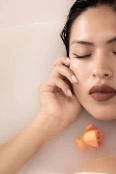 A serene woman with closed eyes relaxing in a milk bath, accompanied by an orange rose for added elegance.